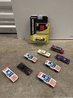 Wide view of all nine die cast cars arranged on the ground including the packed GreenLight IndyCar collectible and various racing/classic cars.