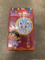 Front view of sealed Dora the Explorer dominoes metal tin with colorful graphics and characters from the show.