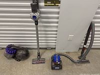 Photo of three Dyson vacuum cleaners: a cordless stick vacuum, a canister vacuum with hose, and a handheld vacuum.