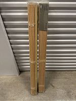 Two unopened packages of IKEA vertical window blinds standing upright on concrete floor, wooden slats visible through plastic wrap.