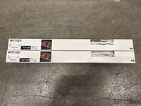 Two sealed boxes of IKEA MITTLED LED light strips on floor, showing logo and package details including length, wattage, and color temperature.
