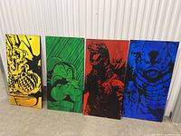 Four large paintings side by side showing characters on yellow, green, red, and blue backgrounds