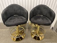 Pair of black upholstered casino style bar stools with gold tone pedestal bases and adjustable height lever.