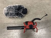 Rode VideoMic microphone with furry wind muff and red shock mount lying on concrete surface.