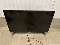 Front view of Seiki 40-inch TV with power cord laid out in front of screen, showing overall condition and TV stand legs.