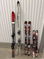 Four pairs of skis from different brands stored vertically showing tops and bindings.