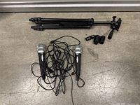Collapsible tripod stand, two wired USB microphones, attached cables, and microphone holders arranged on the ground