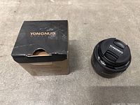 Black Yongnuo branded camera lens with cap beside original box showing the brand.