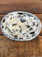 Top-down view showing mosaic abalone shell inlay pieces forming the inside surface of the oval decorative bowl.