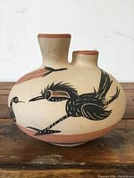 Side view of the pottery jug showing the painted black bird with extended wings and a grain stalk motif.