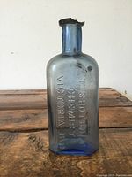 Full view of the antique blue glass chemist bottle showing embossed text and shape