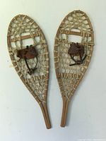 Pair of small antique snowshoes with wooden frames, rawhide webbing, and leather strap bindings, shown from top view.