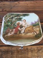 Top view of lidded porcelain box showing detailed painting of a couple and sheep in pastoral scene.