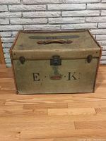 Front view of the antique traveling case with leather handle and metal latch, showing 'E.K.' stencil and surface wear.