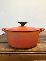 Front view of orange round cast iron pot with lid, showing handles and black knob on lid.