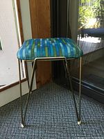 Side view of the stool showing the turquoise metal frame and multicolor patterned cushion.