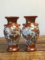 Front view of the pair of vases showing floral and bird decorations and orange-gold neck and bases.