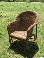 Side view of solid rattan rocking chair showing curved backrest and woven seat on grassy outdoor setting.