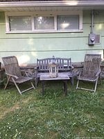 Front view of the full set including wooden bench, two chairs, table, and lantern on grass in front of house wall