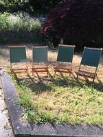Four low child's outdoor chairs lined up on grass showing wooden slat seats and green cloth backs under sunlight.