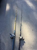 Full view of both fishing rods with reels on pavement.
