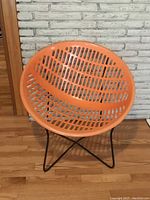 Front view of vintage orange plastic chair with vented seat and black metal crisscross legs, showing overall design and condition.