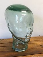 Clear heavy glass mannequin head shown from front angle on wooden surface