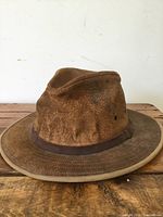 Front and side view of a brown vintage leather hat showing wear and discoloration on the leather.