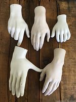 Five white vintage mannequin hands of various sizes laid out on a wooden surface, showing overall wear and vintage condition.