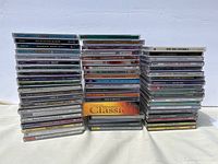 Three stacks of music CDs arranged side by side, showing the front spine and some cover artwork of the CDs. The left stack shows various titles such as "Let's Go on with the Dance" and "Dance Mix". The middle stack includes a bright orange CD titled "2001 Morrison Classics". The right stack contains music including classical titles like "Mozart" and "Rachmaninov".