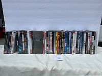 View of 32 DVD movie cases standing upright showing spines and covers with various movie titles, including a Warner Bros. collector's edition case.