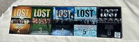 Five DVD box sets of Lost seasons 2 through 6 aligned left to right, showing cover art with season numbers and distinct colors.