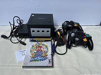 Front view of Nintendo GameCube console, two controllers, sealed Super Mario Sunshine game, and cables