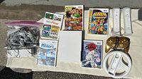 Wii console lot showing console, games, controllers, and cables laid out on a white cloth surface.