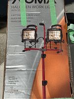 Box showing two 500W halogen work lights on adjustable red tripod stand, front view with packaging details and condition visible.