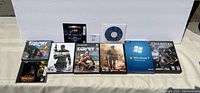 Photo showing 10 PC game and software titles lined up, including Far Cry, Call of Duty, Warcraft III, StarCraft II, Windows 7, and a blank CD in a sleeve.
