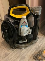 Front view of cleaned unit with power cord coiled, bottle of cleaning formula and attached cleaning wand with spray trigger