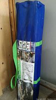Blue storage bag with green straps containing the Entipede Centipede Folding Sawhorse, label showing product images and specifications attached.