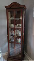 Frontal view of the china cabinet showing the wood finish, glass door, and interior glass shelves with display items removed as per seller.