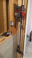 Full assembled vacuum hanging on wall mount beside two loose attachments on bench