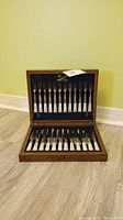 Full view of the open wooden case showing twelve forks and twelve spreaders with mother of pearl handles inside.