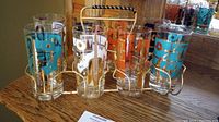 Full set of eight tall drinking glasses with colorful music-themed designs in the gold-tone metal caddy.