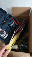 Box with hand tools including screwdrivers and pliers, metal clamp and other items.