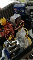 Photo showing boxed HeathZenith motion activated LED light, LED floodlight, and other boxed items in background with extension cords and power stapler in foreground.