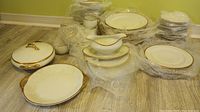 Overview of Limoges Elite Works china wrapped in protective bubble wrap showing various plates, teacups, covered tureen and gravy dish, all cream colored with gold band.