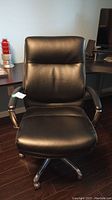 Front view of black vinyl office chair with padded seat and backrest on caster base.