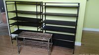 Three large black metal and plastic strip shelving shoe racks with stacked design and one smaller wooden shelf unit with metal legs in front.