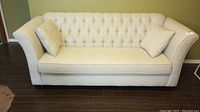 Front view of beige tufted back sofa with curved arms and two throw cushions
