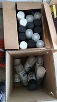 Photo of spray paint cans in two open cardboard boxes showing cans in white, black, and clear caps.