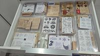 Drawer with multiple sets of wood mounted rubber stamps and two small spray bottles of stamp cleaner.